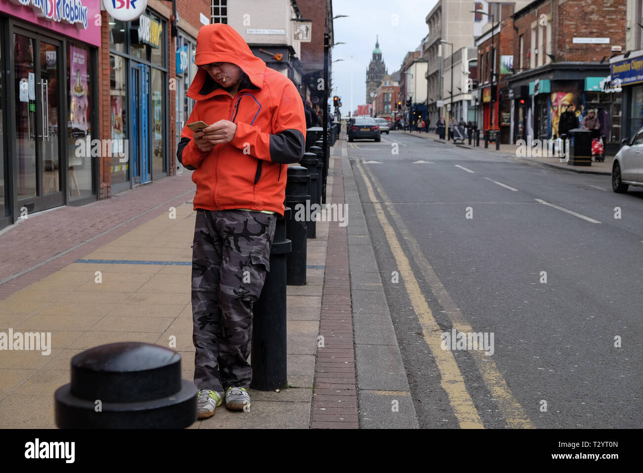 bollard cigarettes Asian man smoking a cigarette and texting on his phone while leaning on a  bollard on a city street Stock Photo