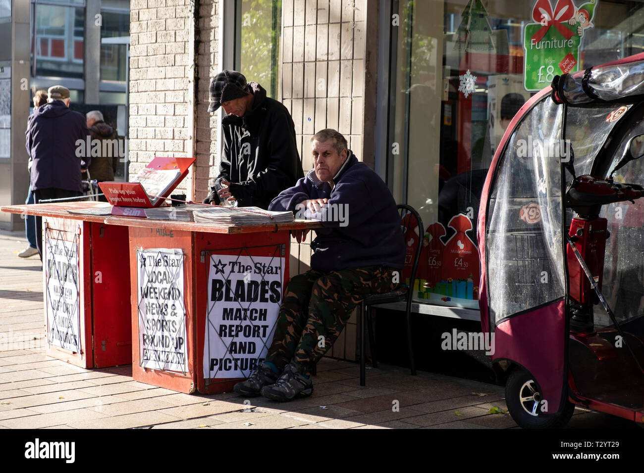 Two men working on a Sheffield Star local newspaper stand on a city street in Winter Stock Photo