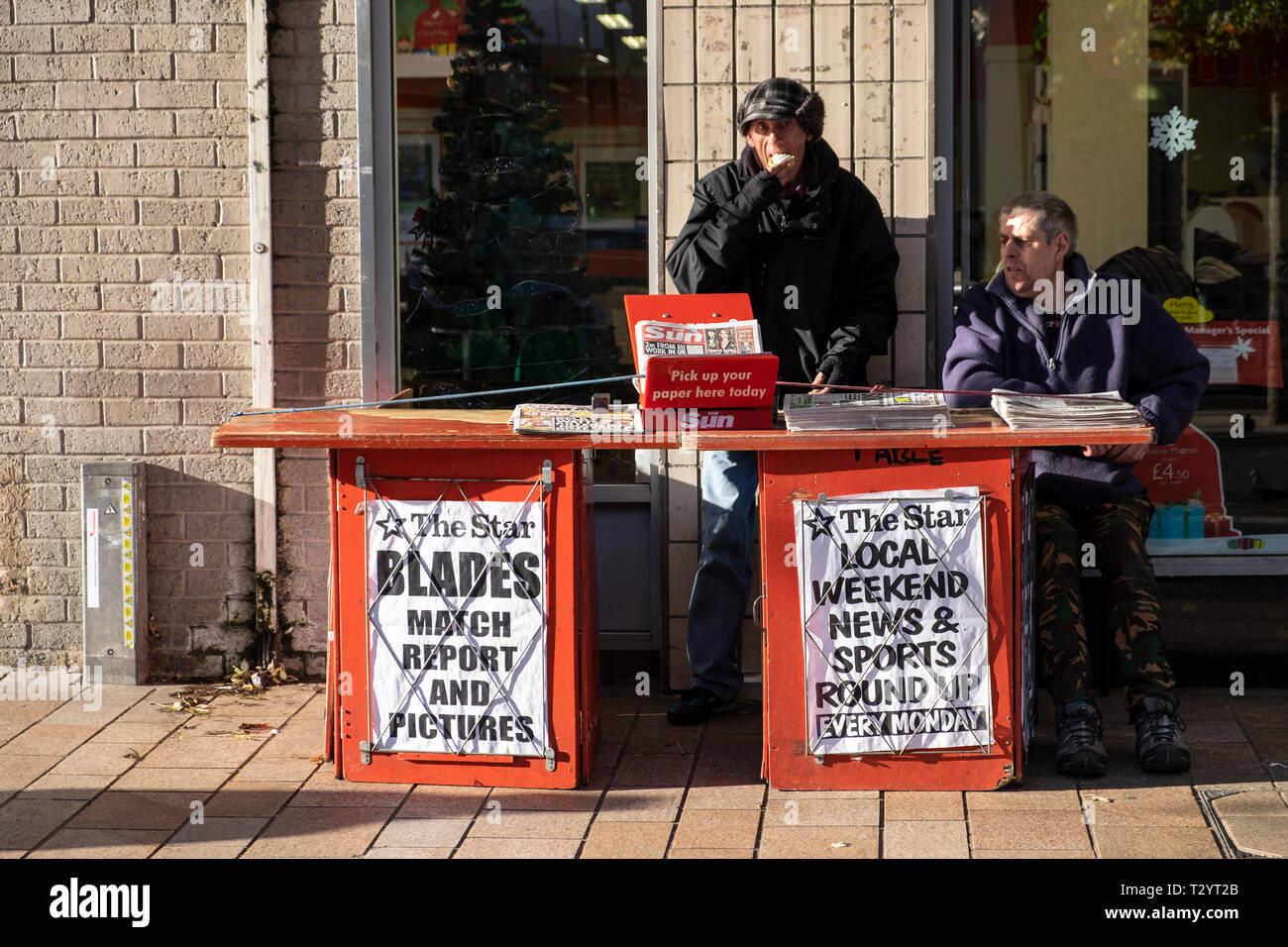 Two men working on a Sheffield Star local newspaper stand on a city street in Winter Stock Photo