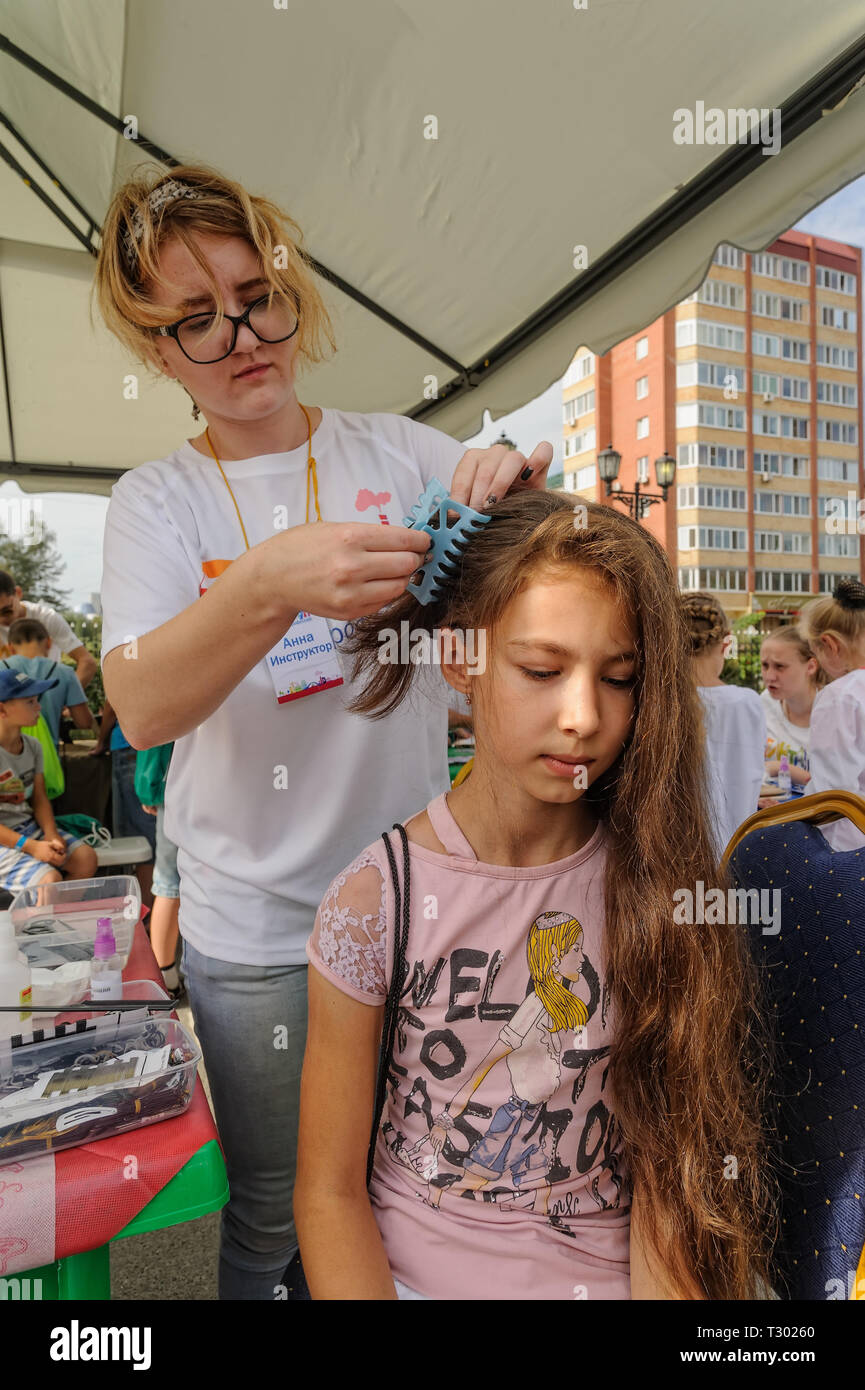 Tyumen, Russia - August 26, 2016: Open Day of Sberbank for children. Young woman hairdresser do hairstyle girl in beauty point Stock Photo