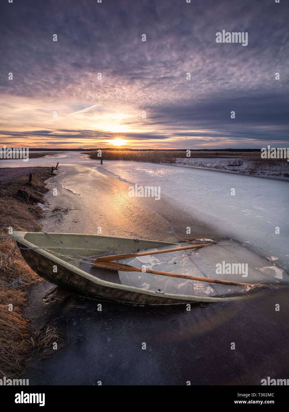Scenic landscape with sunset and abandoned boat at spring evening in Finland. Boat is almoust in the ice. Stock Photo