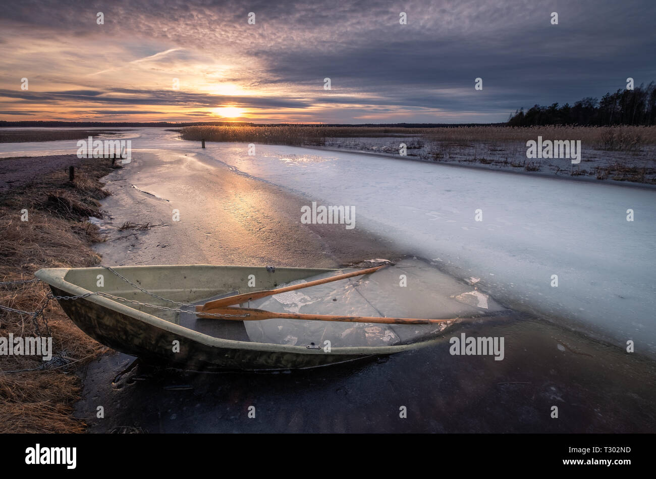 Scenic landscape with sunset and abandoned boat at spring evening in Finland. Boat is almoust in the ice. Stock Photo