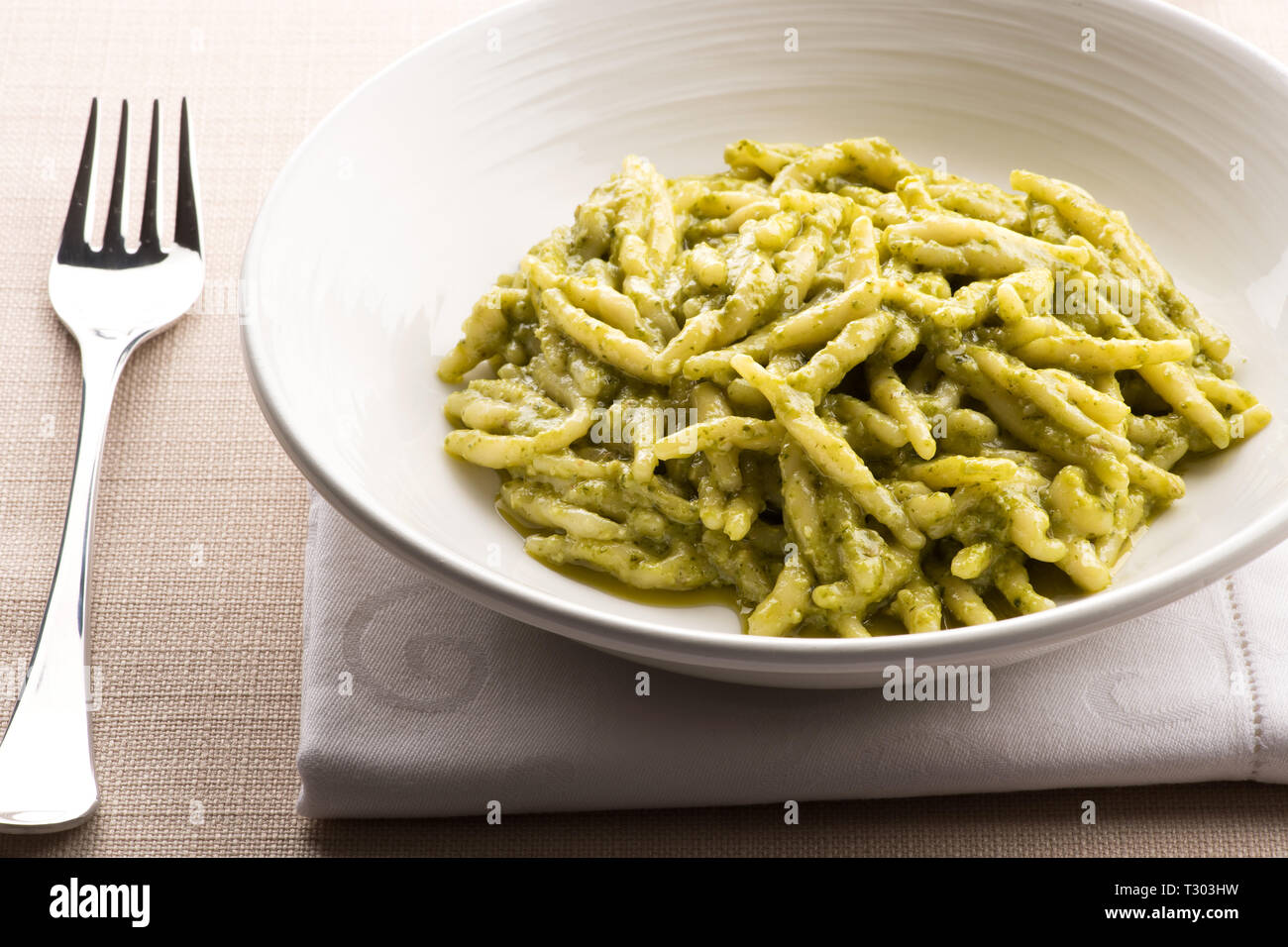 Ligurian trofie pasta, Trofie al pesto, with fresh pesto sauce served as an appetizer in a white bowl with napkin and fork for traditional regional It Stock Photo