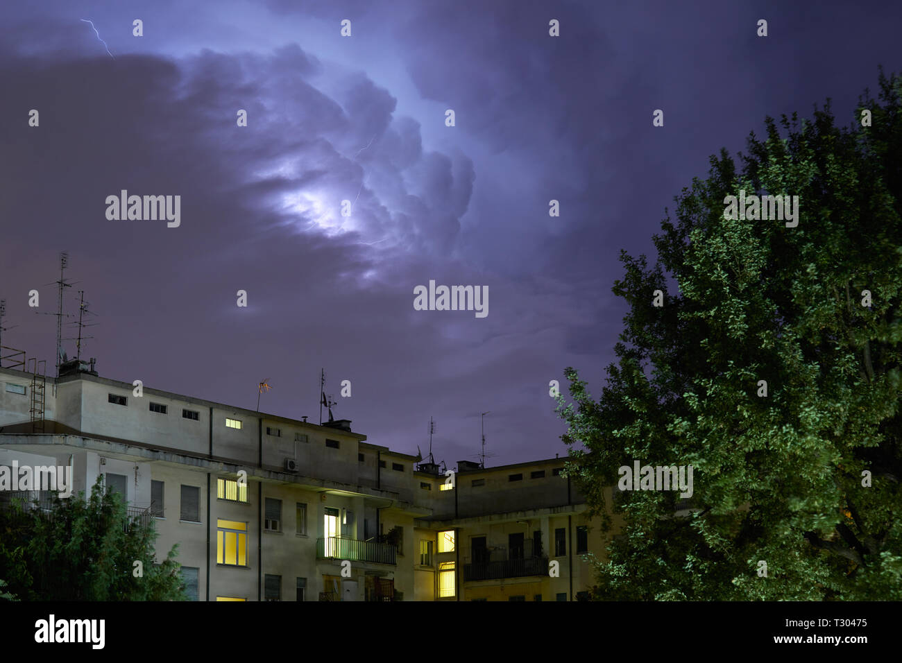 Buildings and green trees at night, illuminated sky during a lightning storm Stock Photo