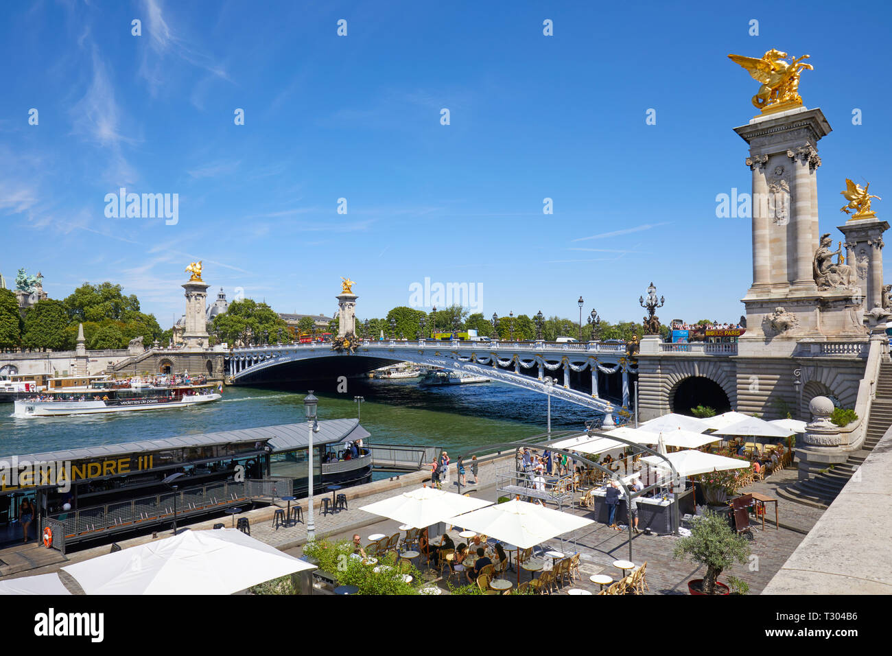PARIS, FRANCE - JULY 21, 2017: Alexander III bridge and cafe in docks area in a sunny summer day, blue sky in Paris, France. Stock Photo