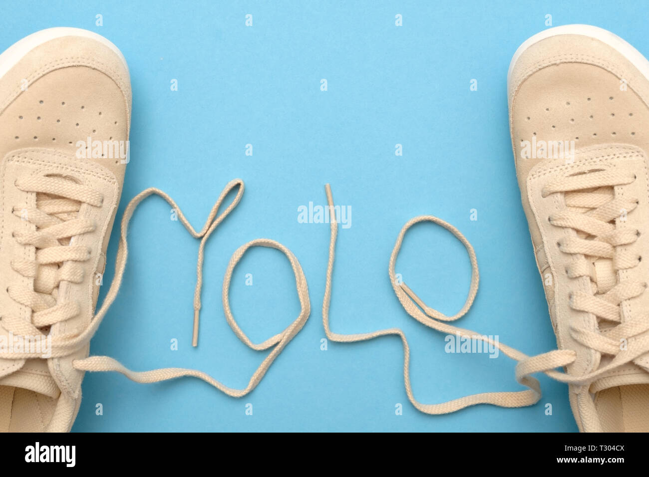 New women sneakers with laces in yolo abbreviation text. Flat lay on blue background. You only live once concept Stock Photo
