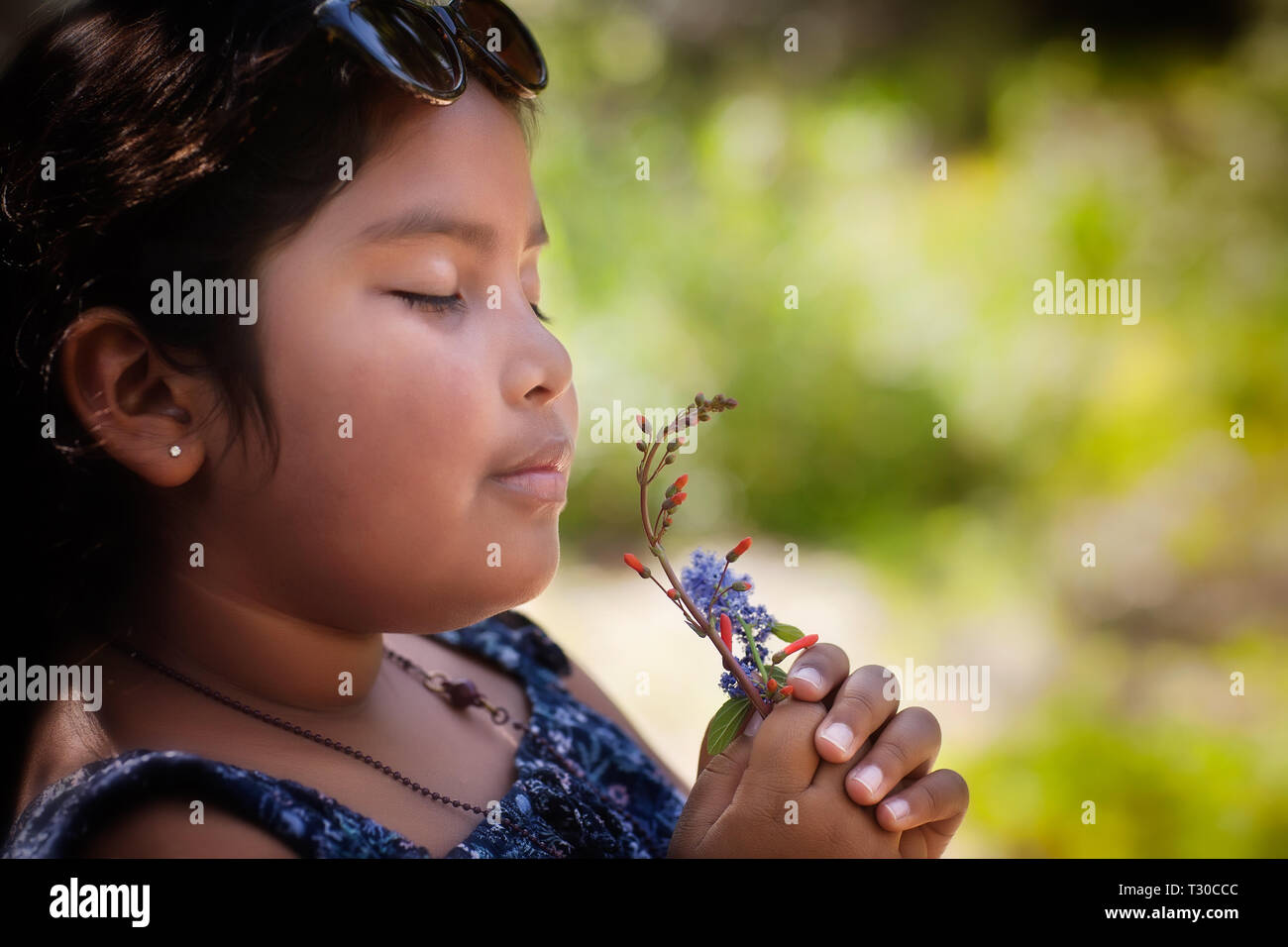 Hispanic little girl with her eyes closed and holding a bouquet of fresh wildflowers to her nose, enjoying the sweet fragrance of the plants. Stock Photo
