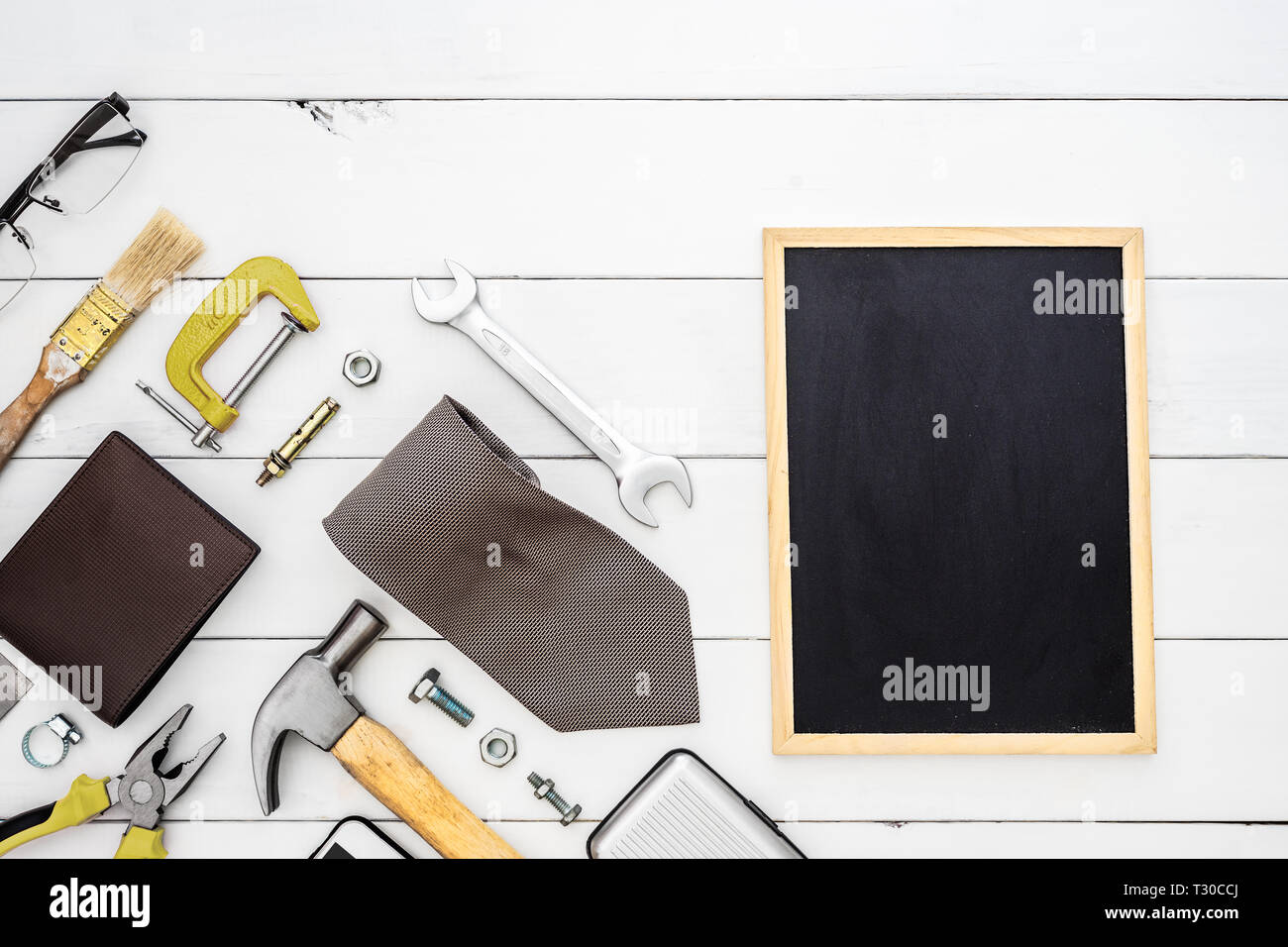 Flat lay of blank space blackboard with construction blue collar handy tools and white collar's accessories over wooden background. Top view with copy Stock Photo