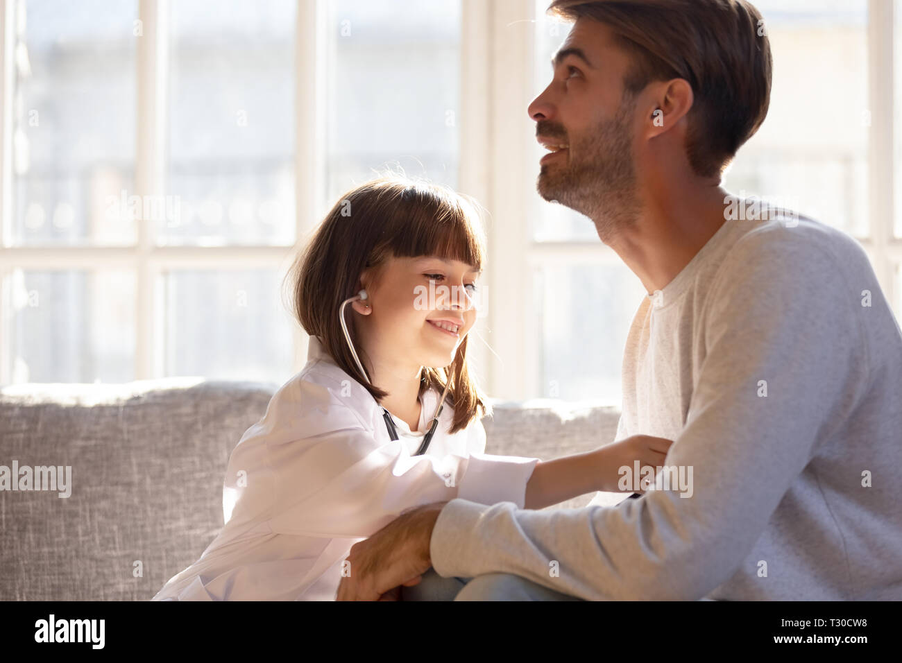 Little girl wearing white coat as doctor play with father Stock Photo