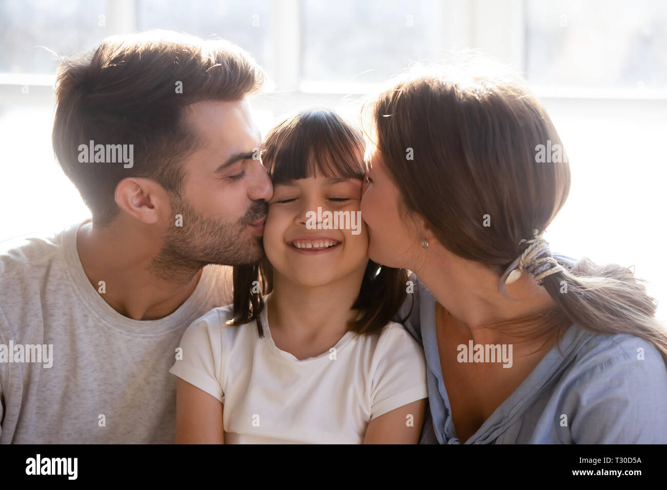 Happy parents kissing little preschool lovely daughter on cheeks Stock Photo