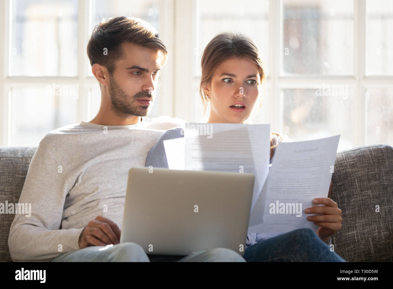 Shocked by bad news couple sitting on couch reading letter Stock Photo