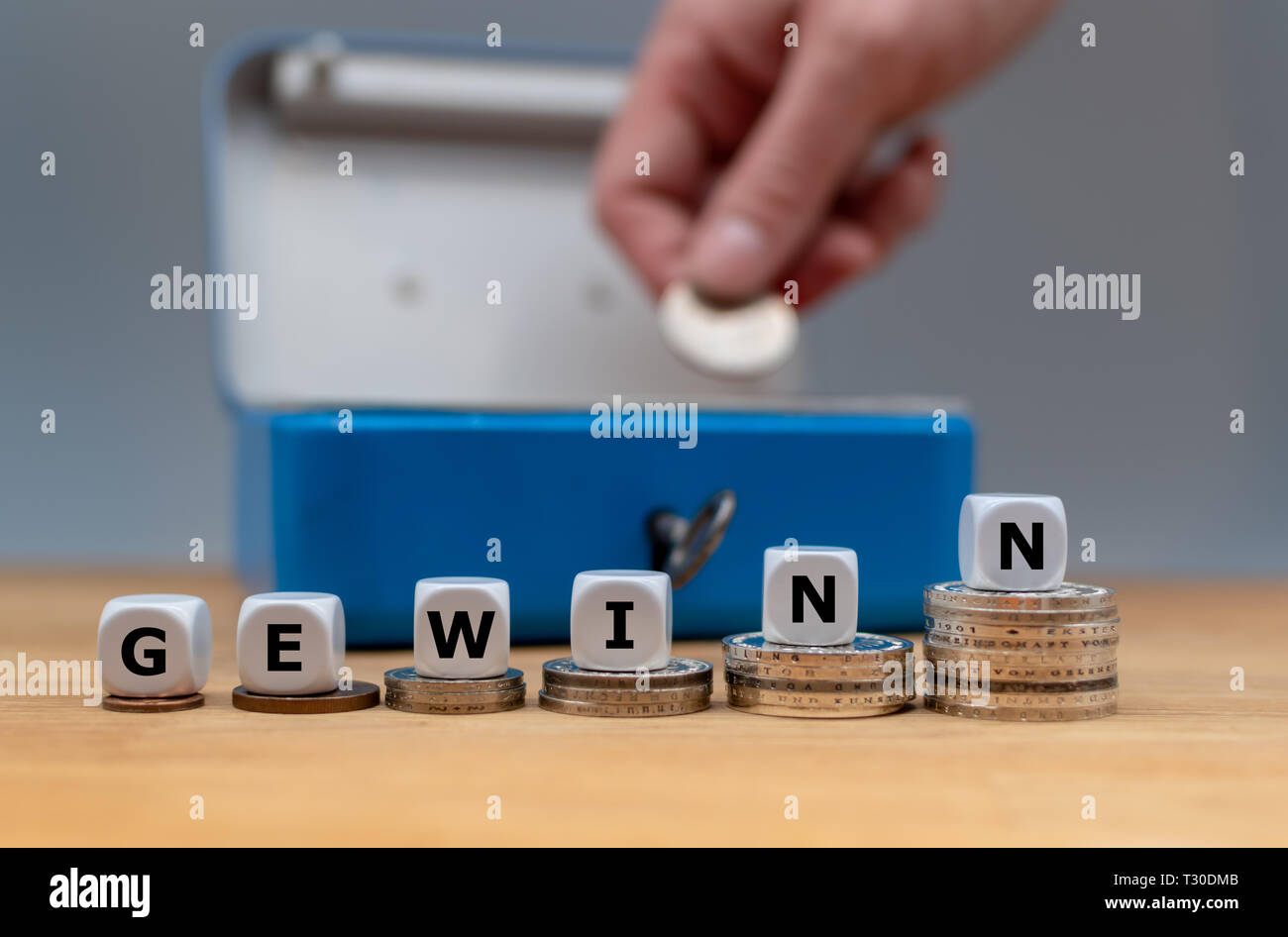 Symbol of increasing profits. Dice form the German word 'Gewinn' ('profit' in English). Dice placed on stacks of coins. A money box is in the backgrou Stock Photo