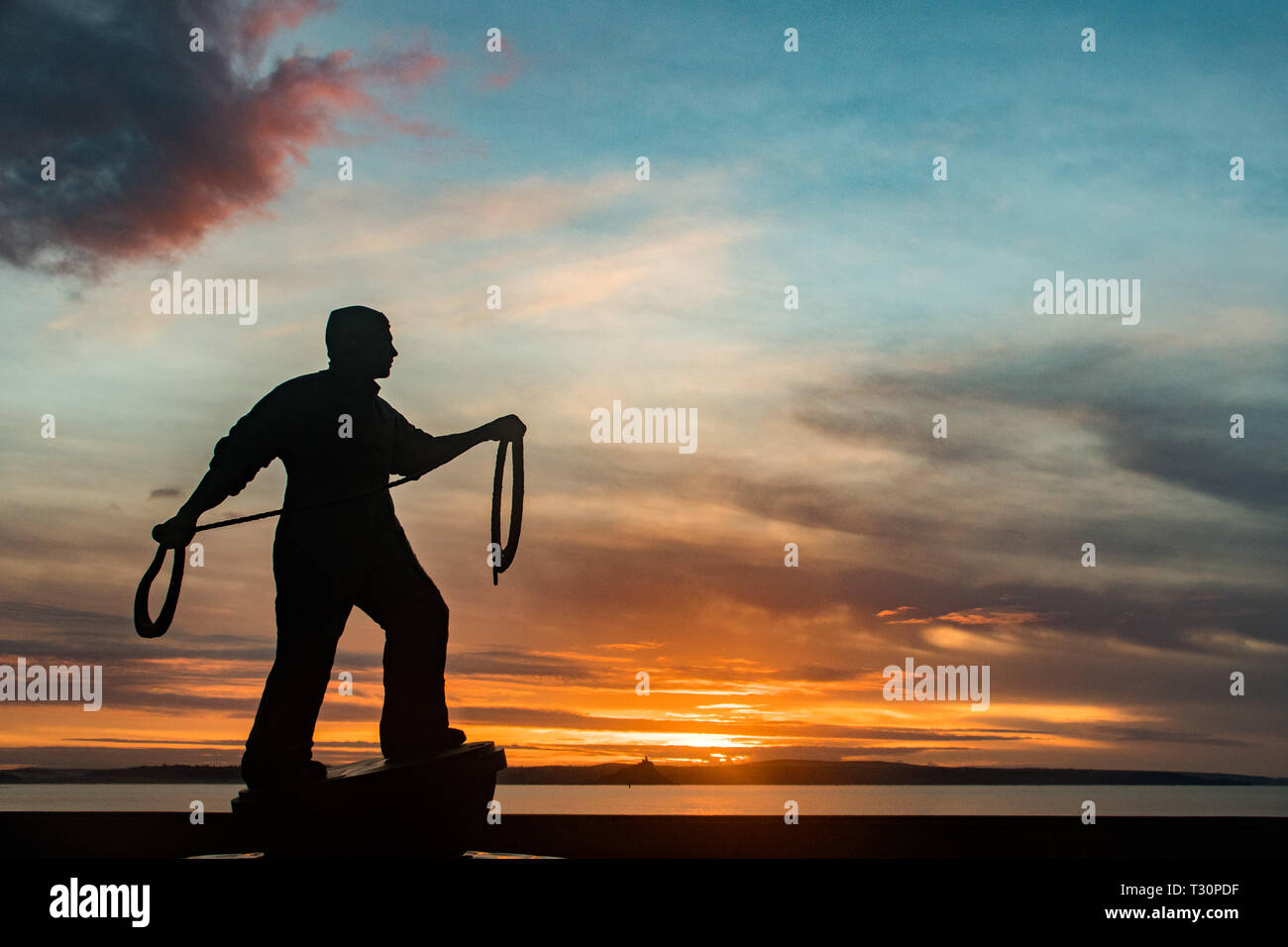 Newlyn, Cornwall, UK. 5th Apr, 2019. UK Weather. A cold but calm and colourful start to the morning at Newlyn looking out to Mounts Bay. Seen here Tom Leapers bronze memorial statue to Newlyn Fishermen silhoutted against the sunrise. Credit: Simon Maycock/Alamy Live News Stock Photo