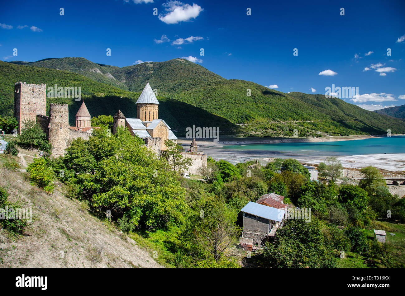Church of the Mother of God, Ananuri with crystall blue Zhinvali reservoir dam in the background and blue sky with few clouds above. Stock Photo