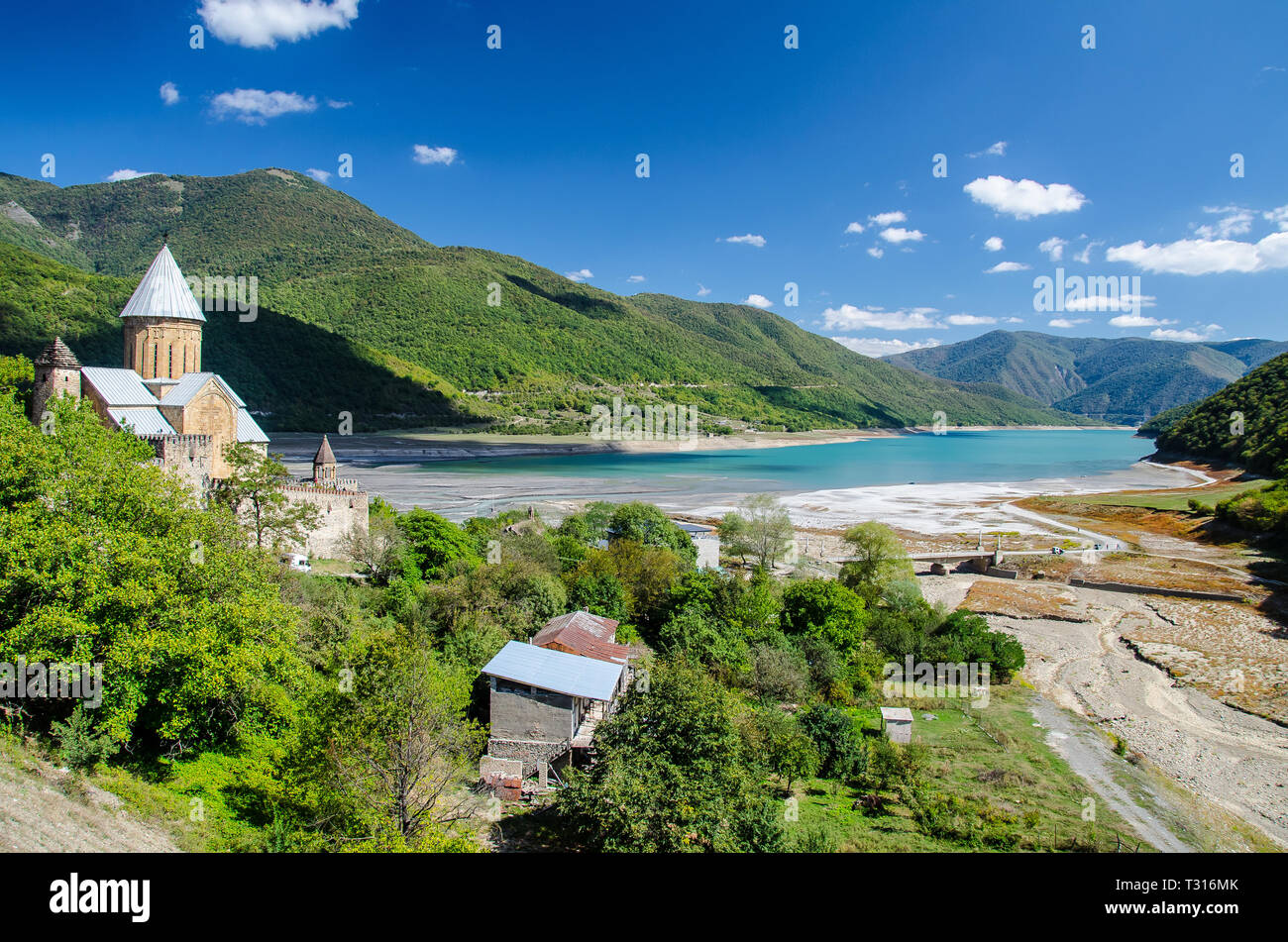 Church of the Mother of God, Ananuri with crystall blue Zhinvali reservoir dam in the background and blue sky with few clouds above. Stock Photo
