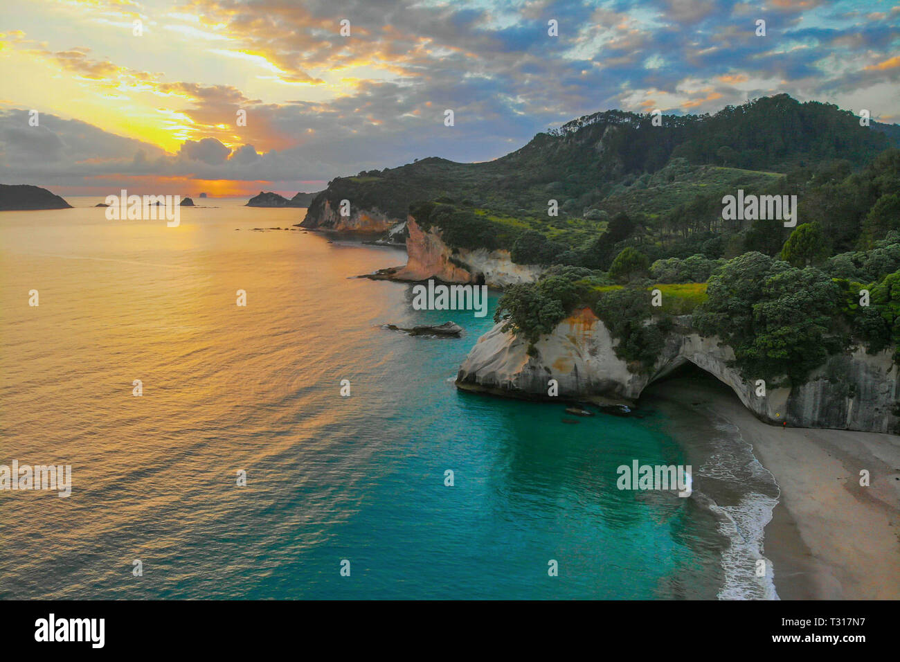 Aerial drone view of Sunrise at Cathedral Cove with blue sky with white clouds above and refelction in the sea, golden hour. Stock Photo