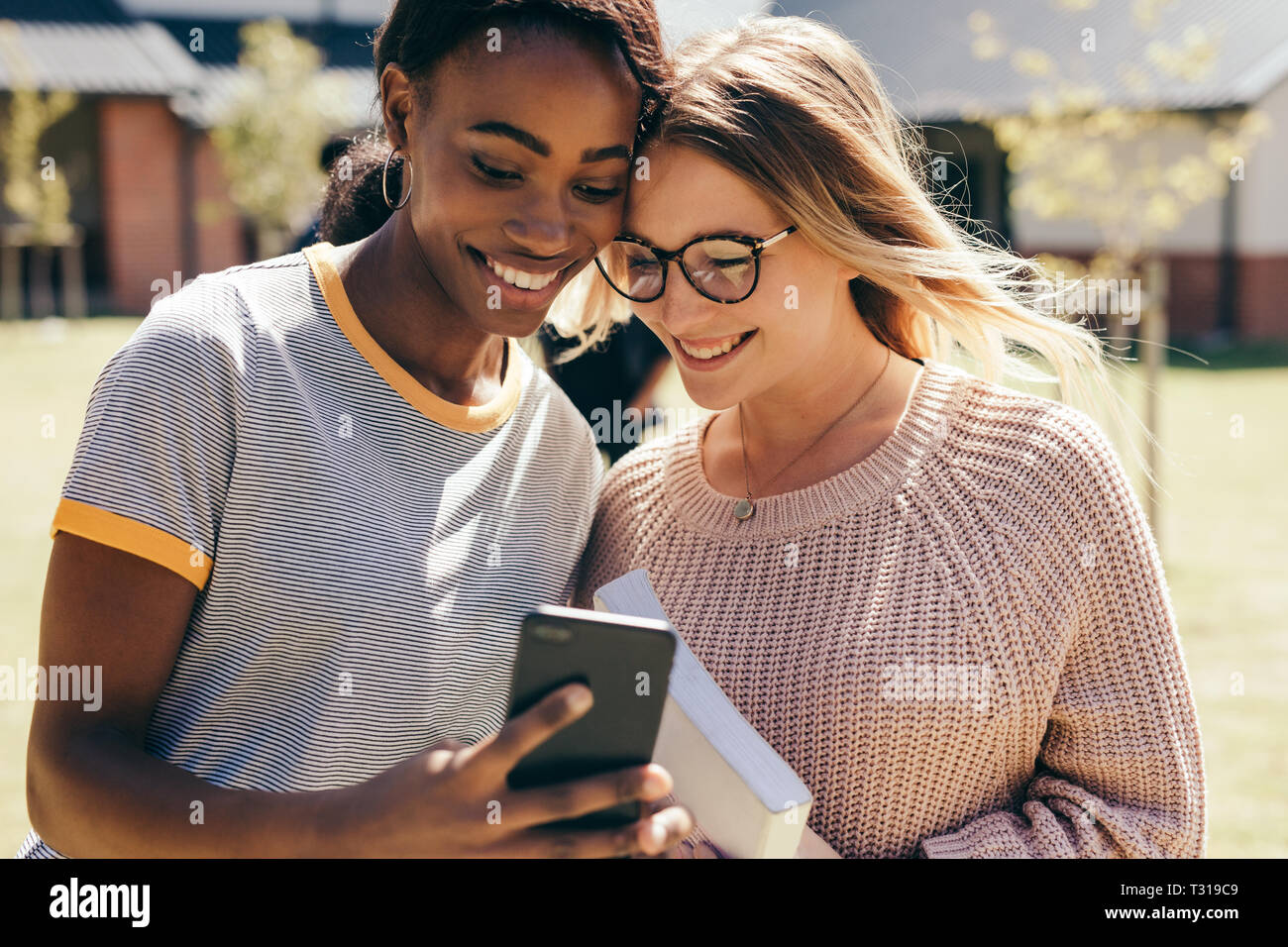 Young women taking selfie with mobile phone at university during break. Two high school girls with mobile phone outdoors in campus. Stock Photo