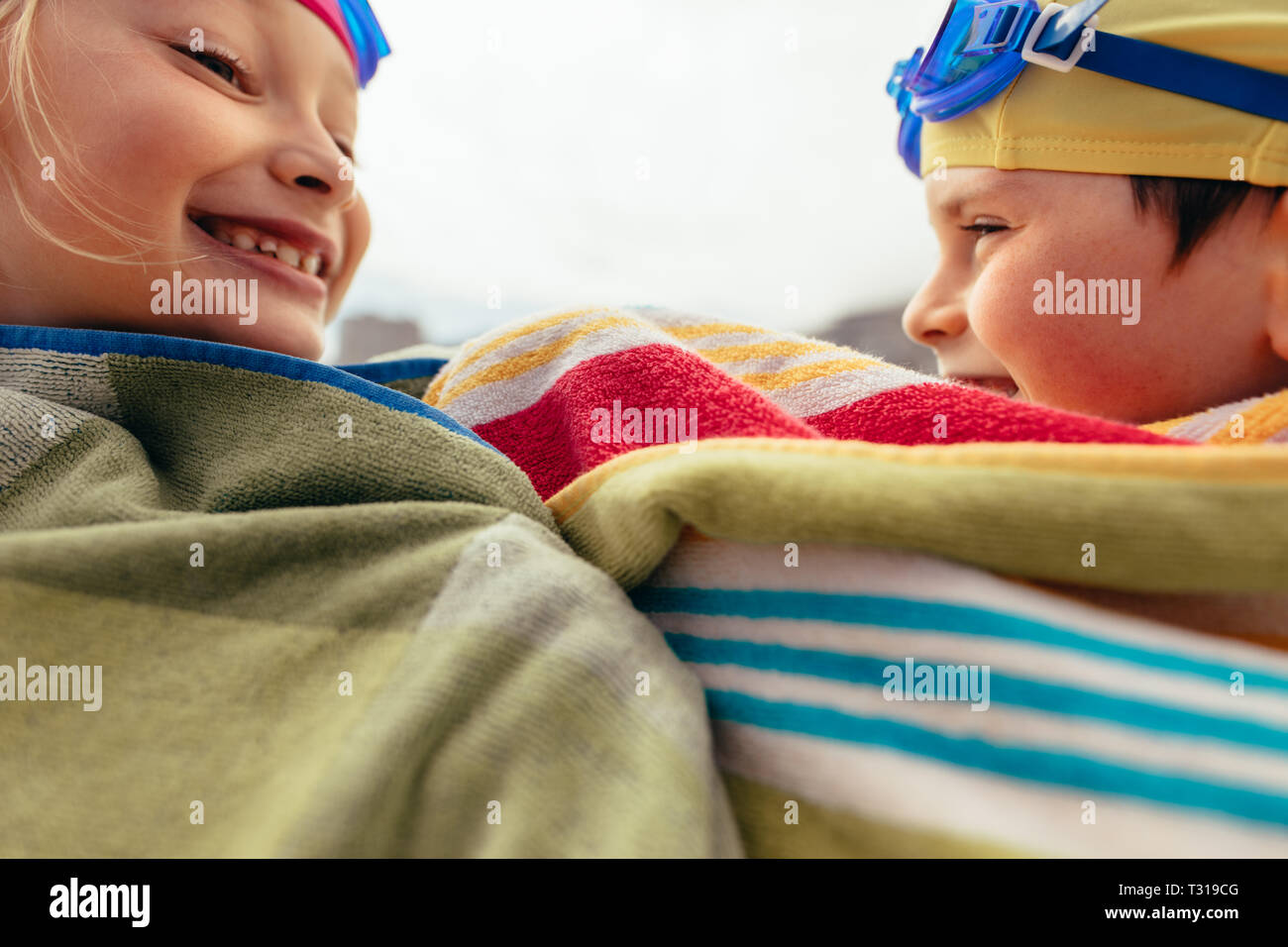 Boy and girl wrapped in towel after swimming training. Two kids having fun after swimming. Stock Photo