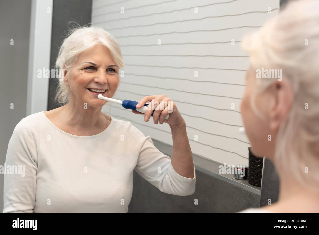 Cute mature woman brushing teeth. Electric toothbrush used by senior woman. Stock Photo