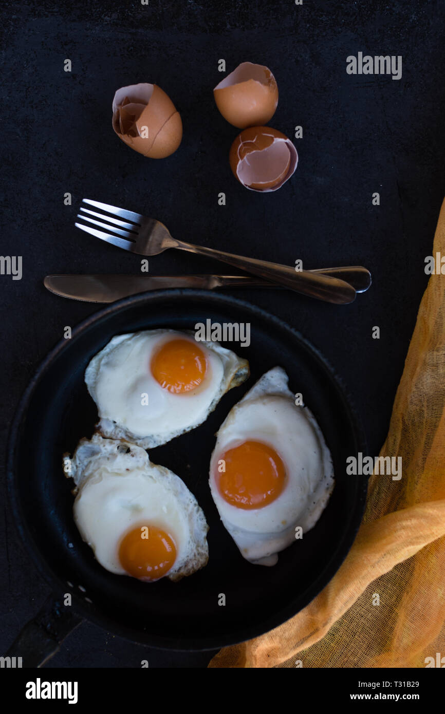 Overhead view of fried eggs in black baking pan on dark background