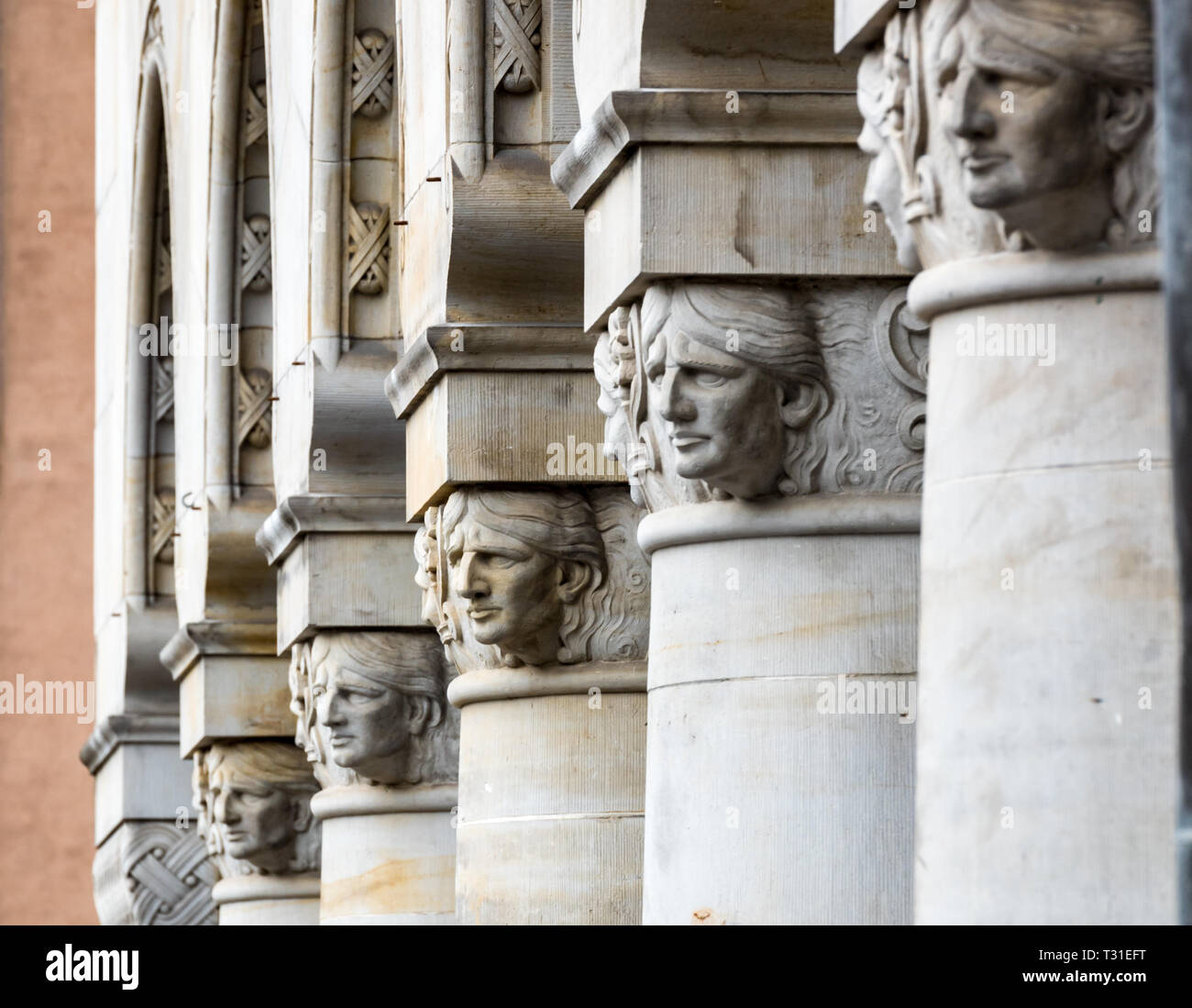 A line of faces look out from the tops of carved stone pillars at Copenhagen City Hall Stock Photo