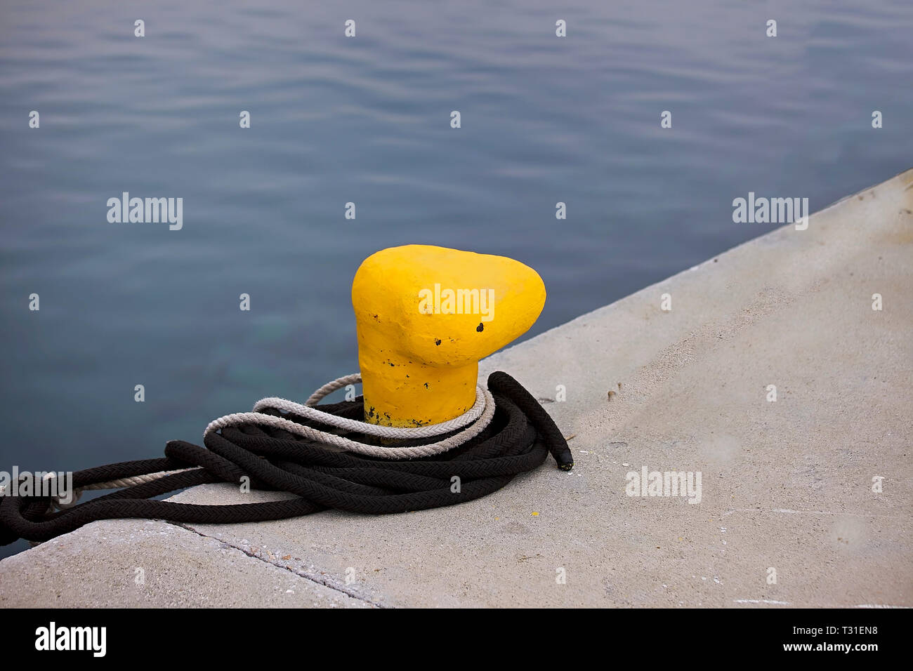 Yellow bollard on the edge of marina with rope. Stock Image Stock Photo