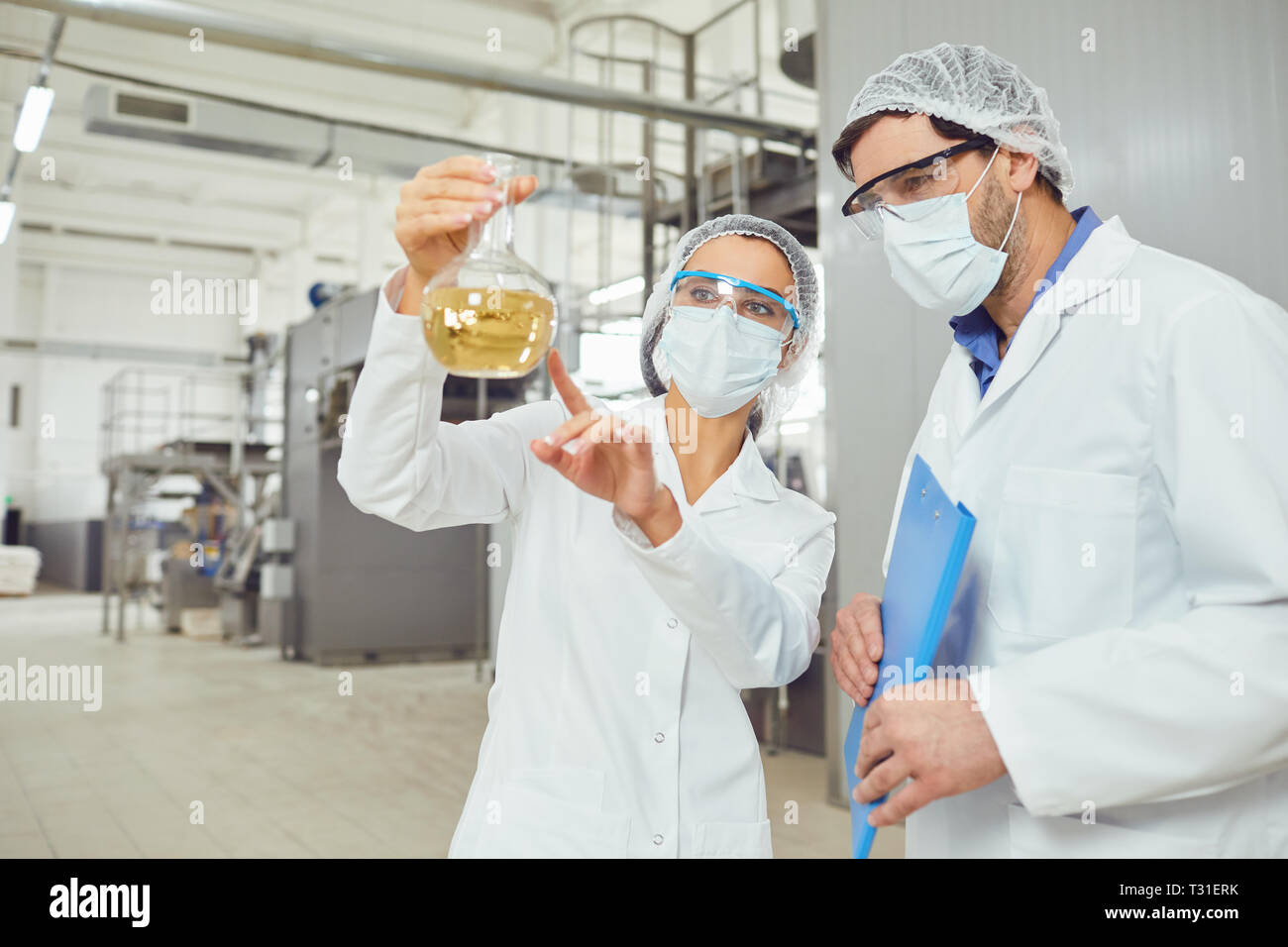 Workers in masks and coats look at the liquid in the flask at work