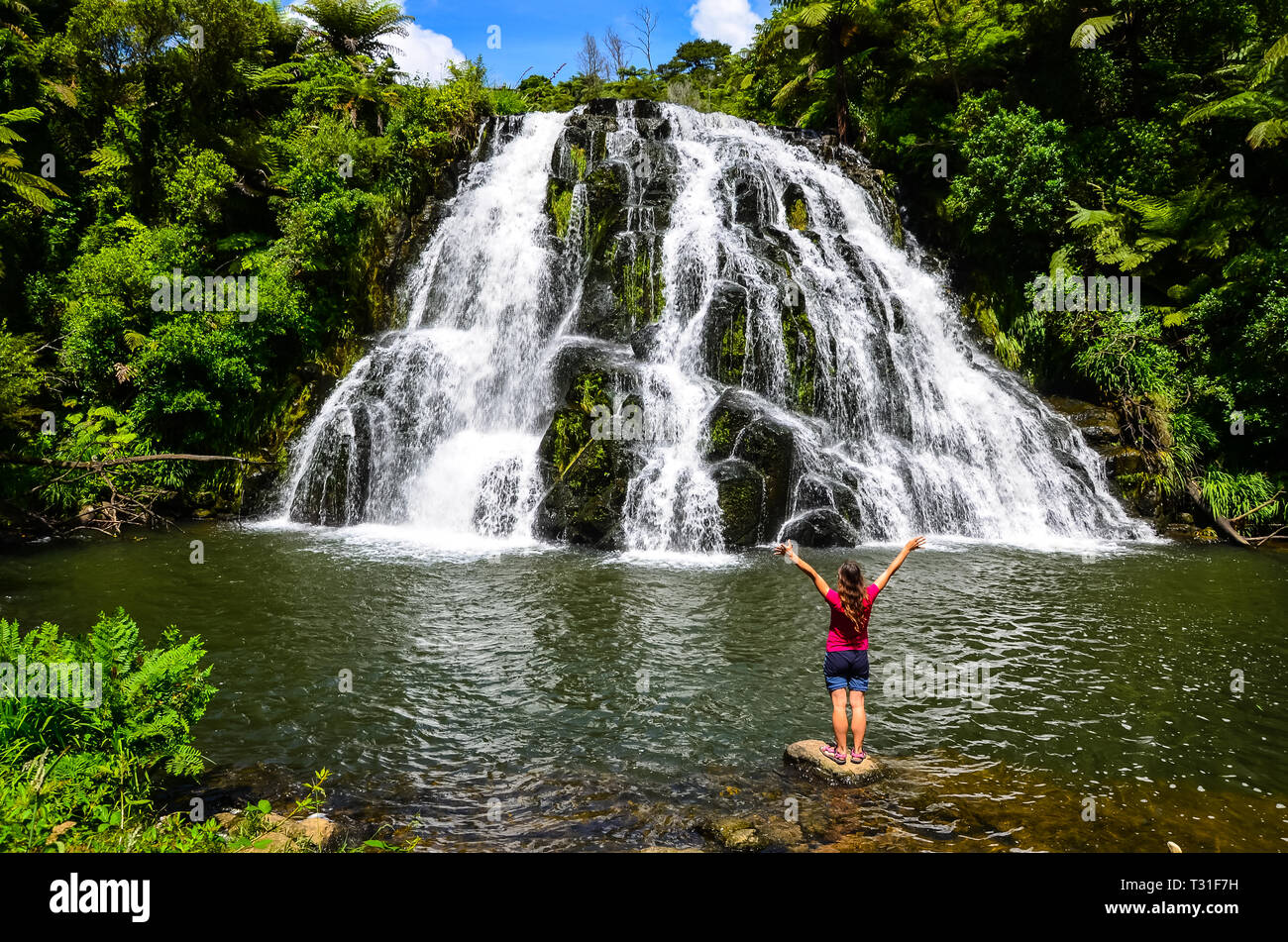 Owharoa Falls with blue sky above and girl tourist person in red t-shirt in the foreground at Coromandel Peninsula, North Island, New Zealand Stock Photo