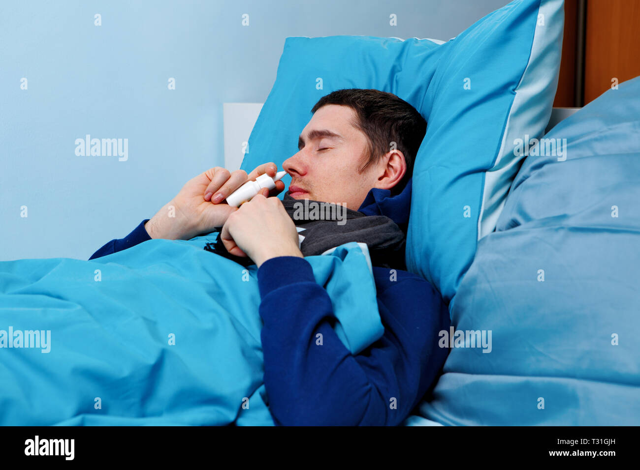 Image of sick man using nasal spray while lying in bed Stock Photo