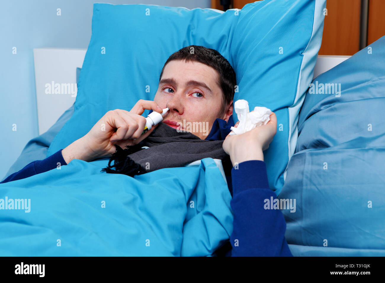 Image of sick man using nasal spray while lying in bed Stock Photo