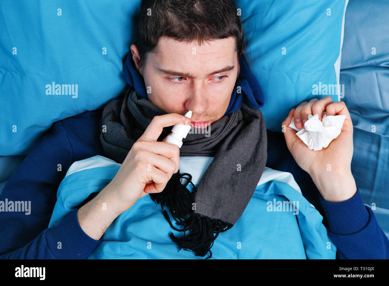 Sick brunet man using nasal spray while lying in bed Stock Photo