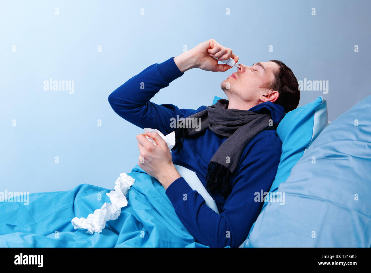 Sick brunet man using nasal spray while lying in bed. Stock Photo