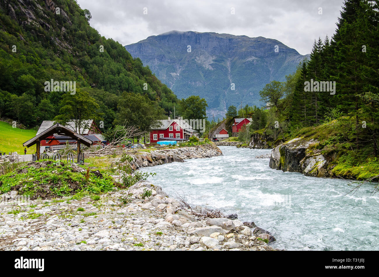 View of a small village with red houses and glacier river in Buarbreen valley in Odda region, Norway. Stock Photo