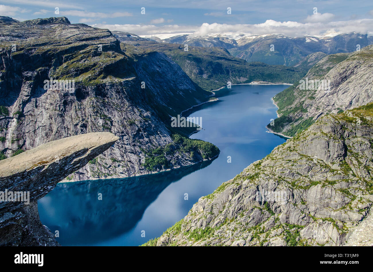 Spectacular view of Trolltunga rock with a blue lake 700 meters lower and interesting sky with few clouds. Stock Photo