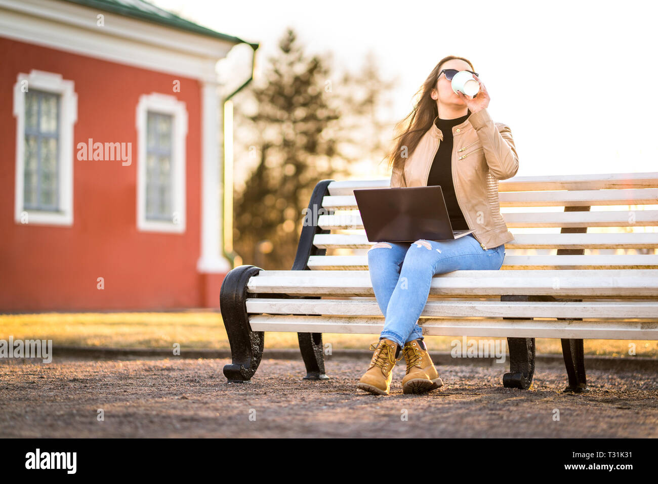 Remote work in outdoor office. Business woman working with laptop in the park or student studying outdoors in campus. Lady drinking coffee. Stock Photo