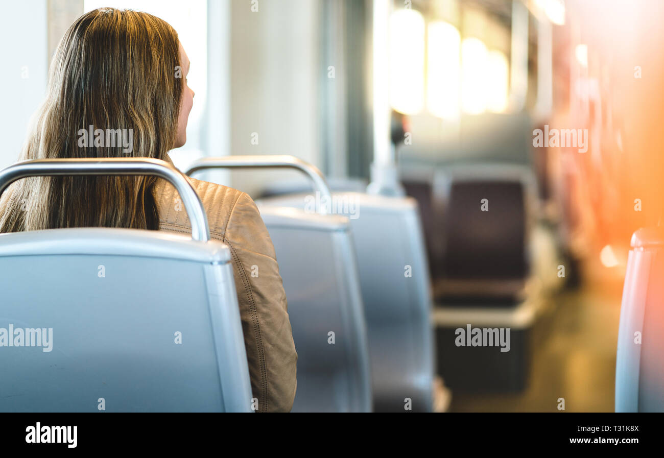 Back view of young woman sitting in public transportation. Passenger riding the bus, train, tram or subway. Happy female traveler. Stock Photo