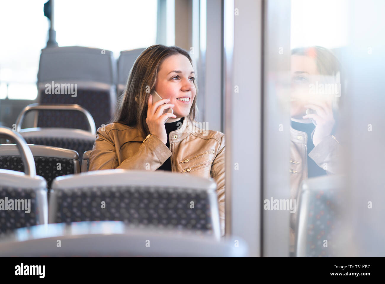 Woman talking on the phone while riding the bus, train, metro or subway. Happy lady with smartphone in public transportation looking out the window. Stock Photo