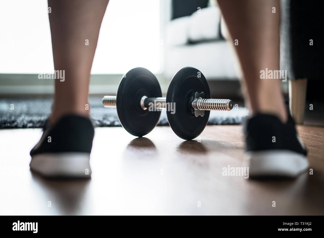 Fitness motivation, determination and challenge concept. Man starting workout and exercise. Muscle training in home gym. Dumbbell between sneakers. Stock Photo