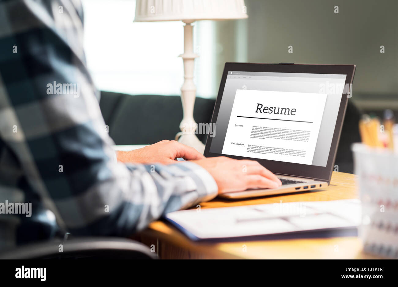 Man writing resume and CV in home office with laptop. Applicant searching for new work and typing curriculum vitae for application. Job seeking. Stock Photo