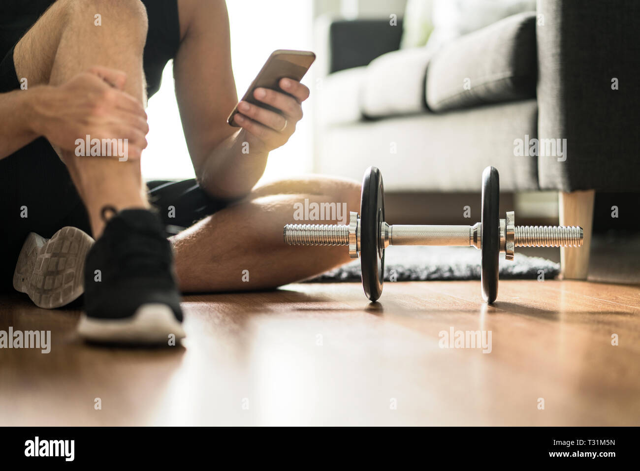 Man using smartphone during workout at home. Online personal trainer or on mobile phone. Internet fitness class or video course. Taking a break. Stock Photo