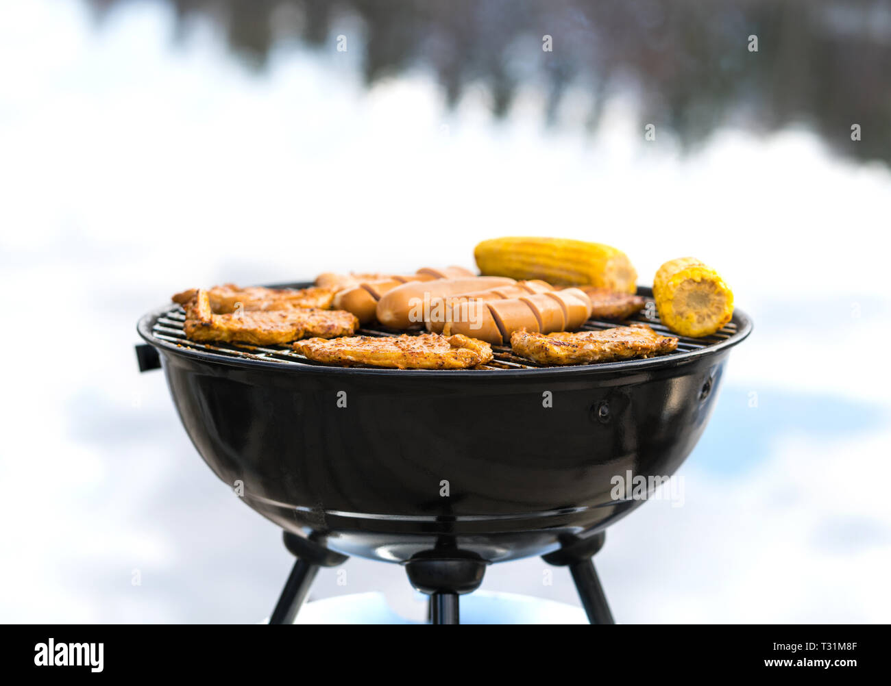 Grilling at the beach. Food cooking on a charcoal kettle grill. Sausages, meat, corn and vegetables in outdoor barbeque in summer. BBQ party. Stock Photo