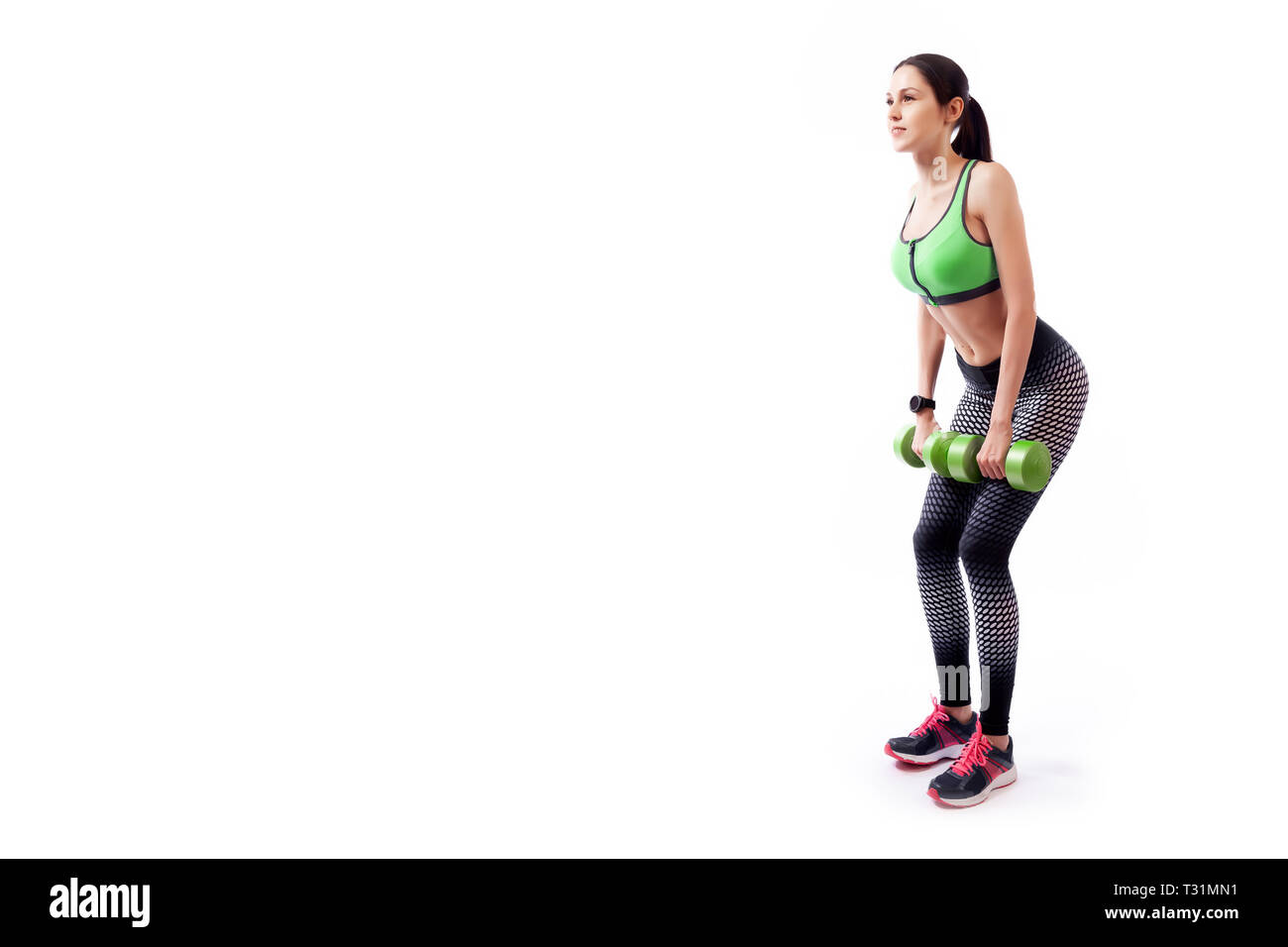 Young woman in sports clothes makes deadlift with weights dumbbell in semi-sitting position on white isolated background. Side view.Fit girl living an Stock Photo