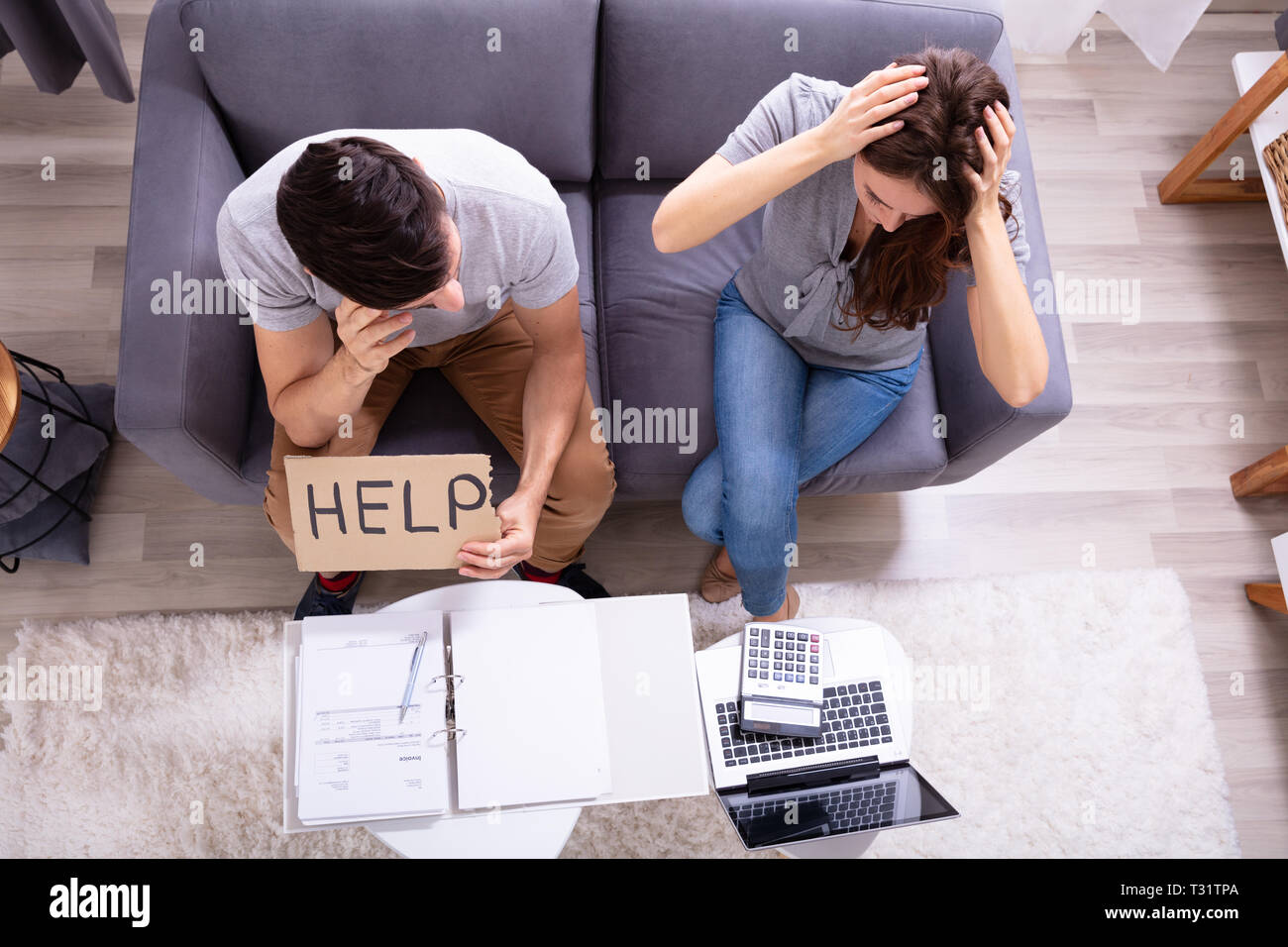 Young Couple Sitting On Sofa Holding Help Sign While Calculating Invoice Stock Photo