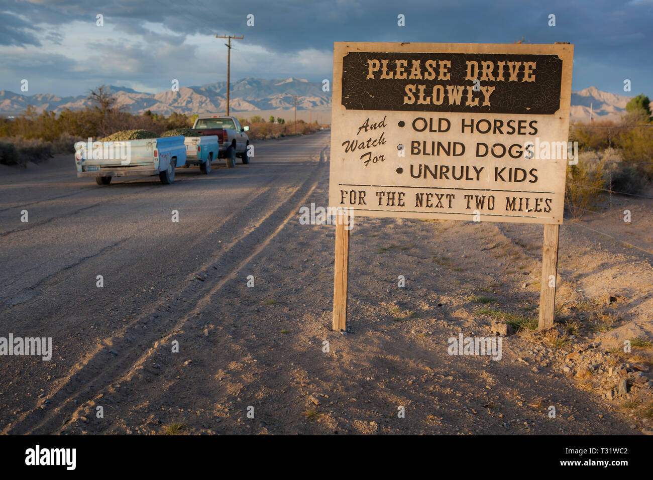 A 'drive slowly' warning sign on desert dirt road with a pickup truck hauling gravel. Stock Photo