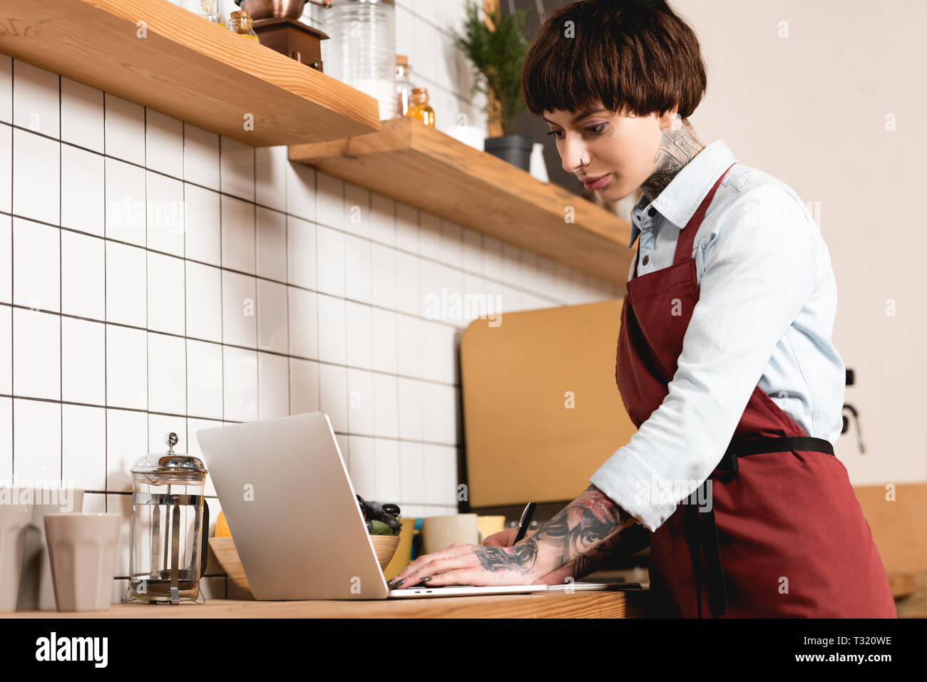 pretty barista in apron using laptop in coffee shop Stock Photo