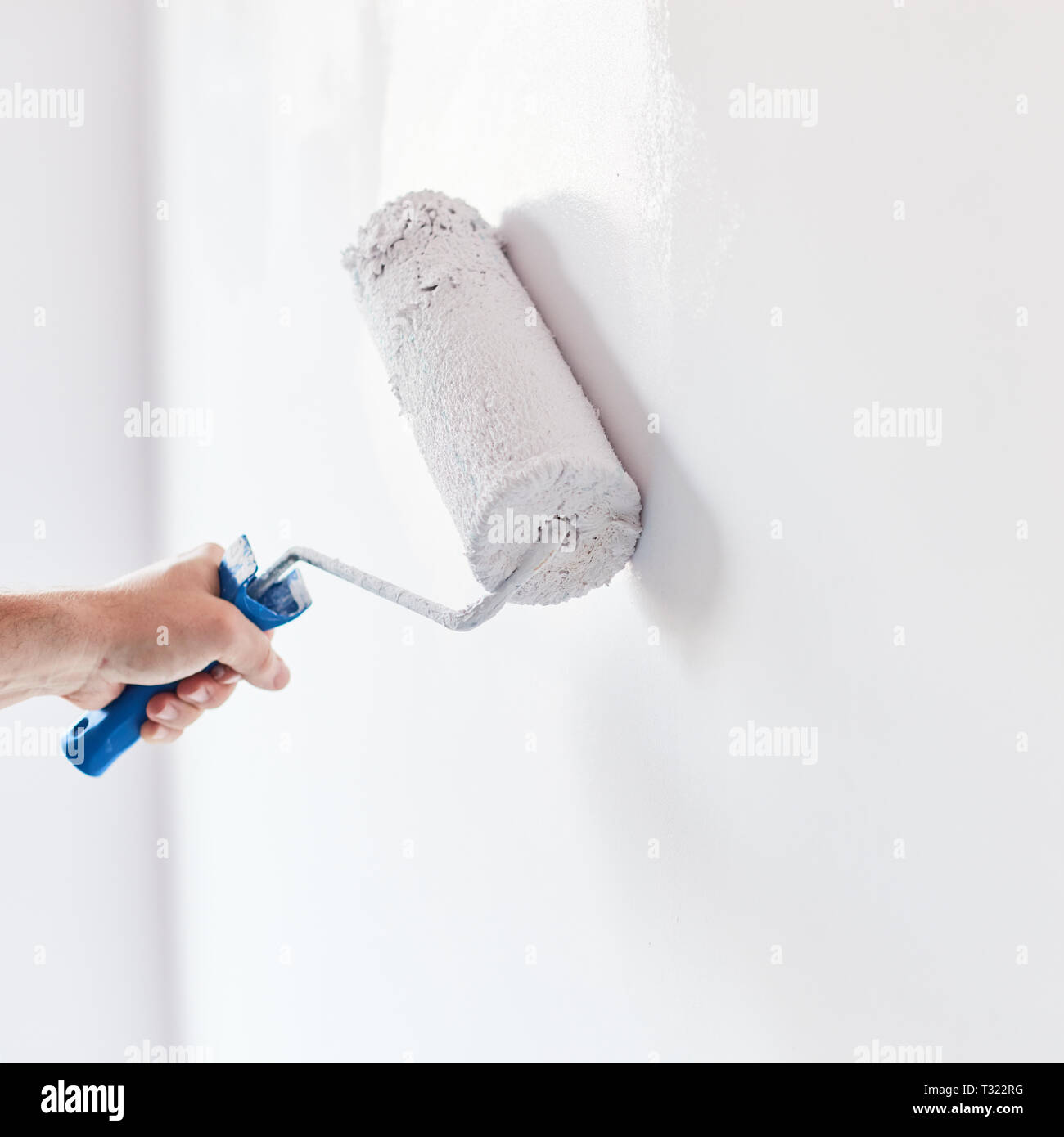 Male hand painting wall with paint roller. Painting apartment, renovating with white color paint Stock Photo