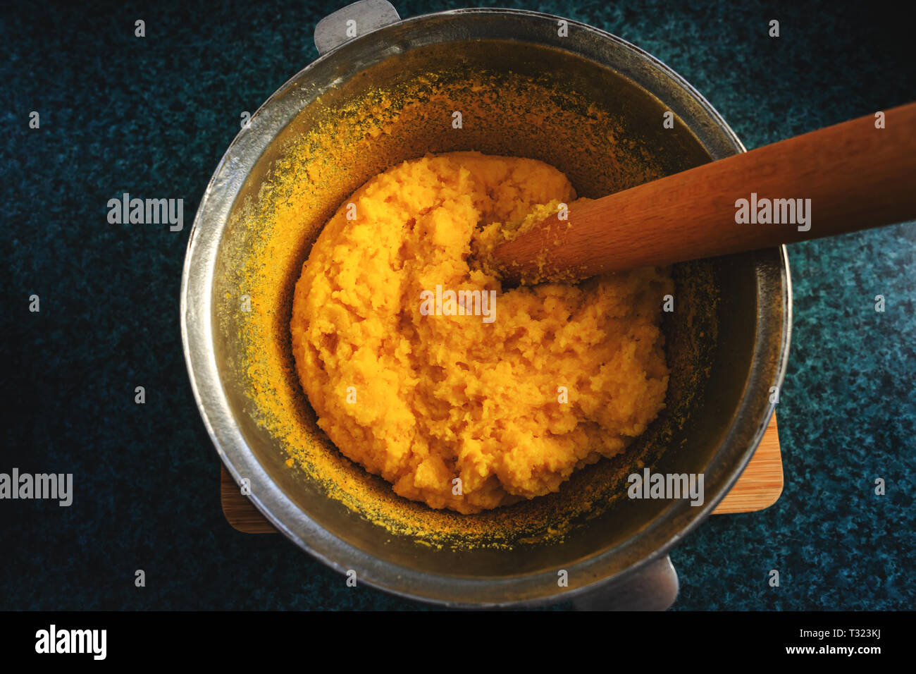 Polenta or mamaliga and beech wood stirrer in cast iron pot (cooper pot).  Traditional dish prepared by boiling water, salt, cornmeal. Substitute for  Stock Photo