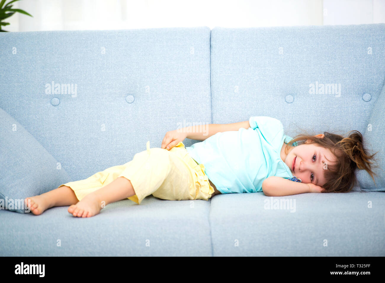 Cute little girl in home clothes lies in the room on the couch Stock ...