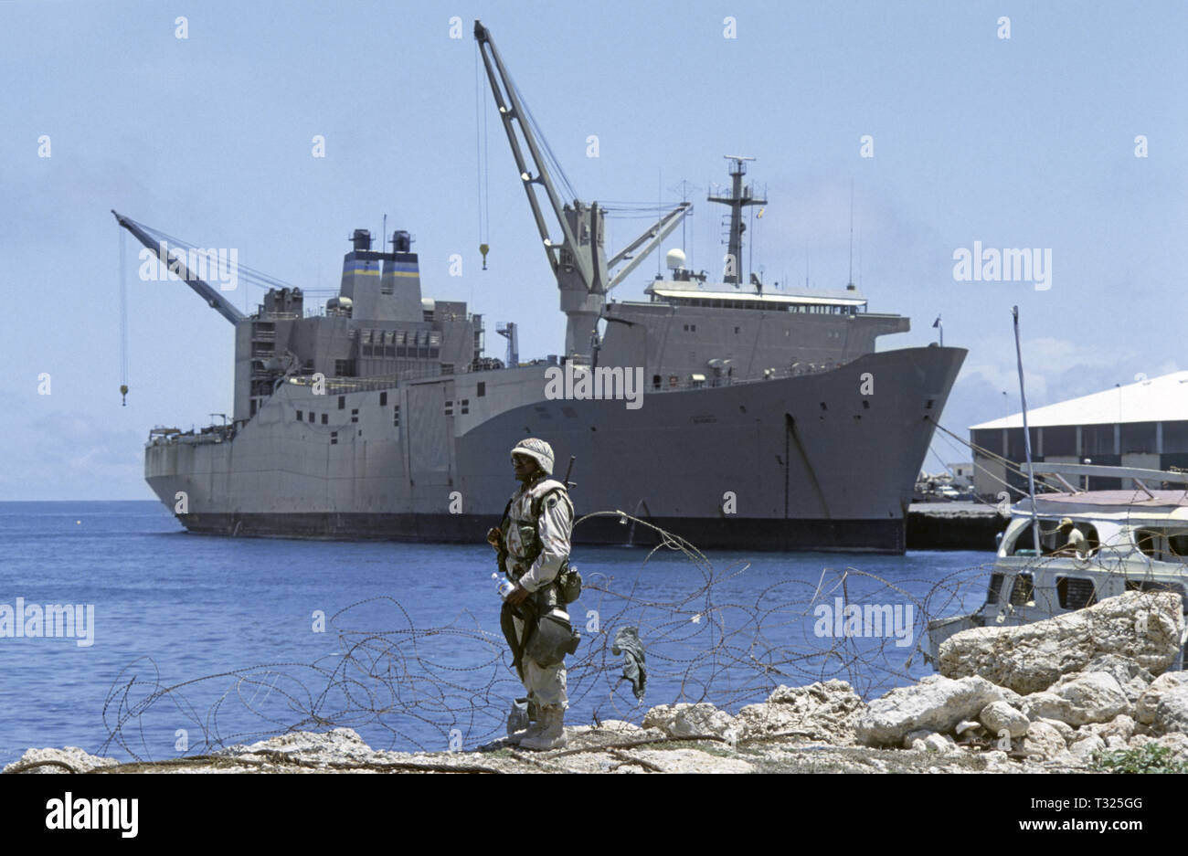 30th October 1993 A black U.S. Army soldier of the 24th Infantry Division, 1st Battalion of the 64th Armored Regiment, stands at the water's edge in the new port in Mogadishu, Somalia. In the background is the huge United States Marine Administration vehicle cargo ship, USNS Denebola. Stock Photo