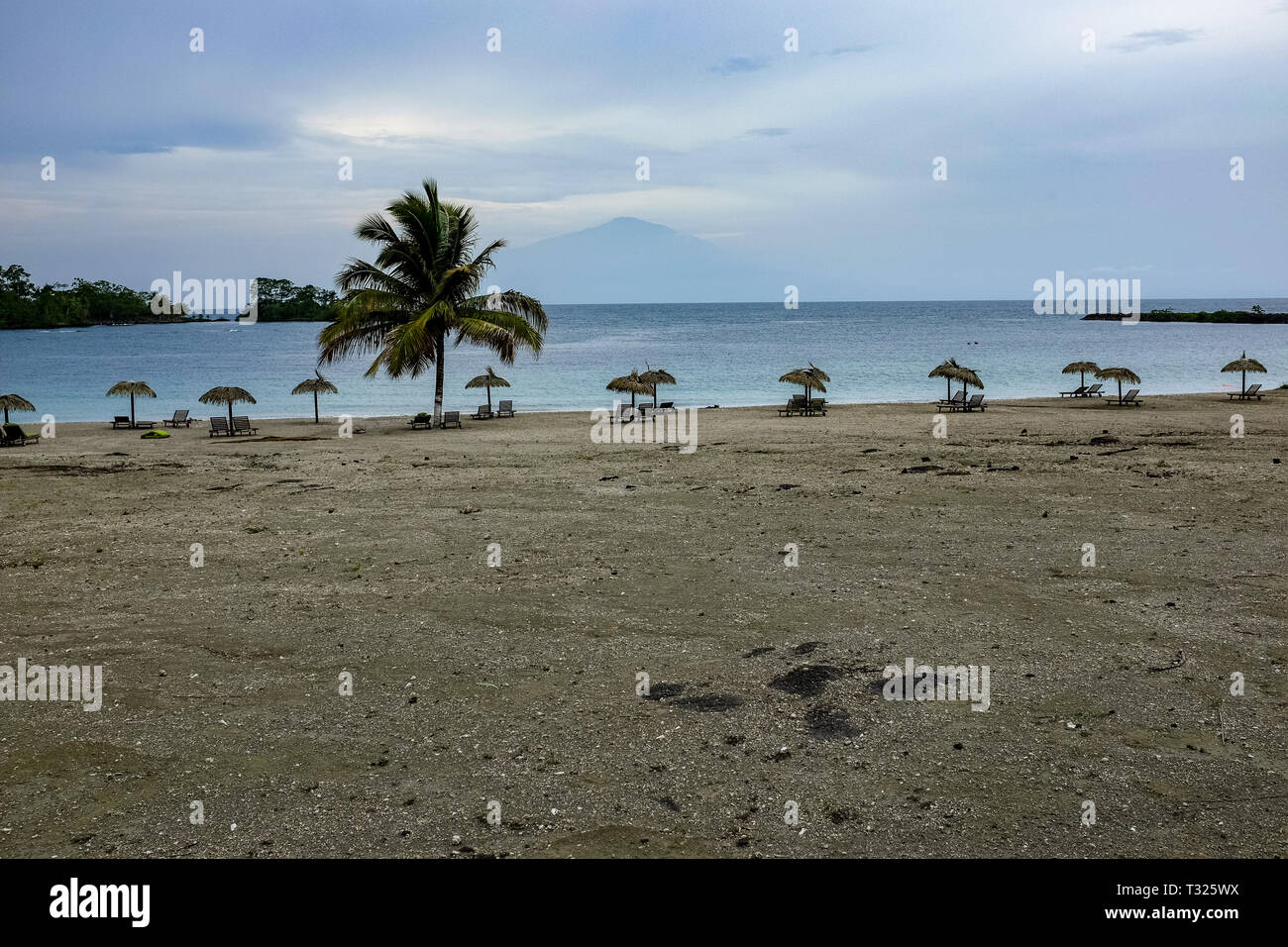 A view of Mount Cameroon from across the sea from Bioko Island, Equatorial Guinea, with a beach, palm trees and sun loungers in the foreground Stock Photo
